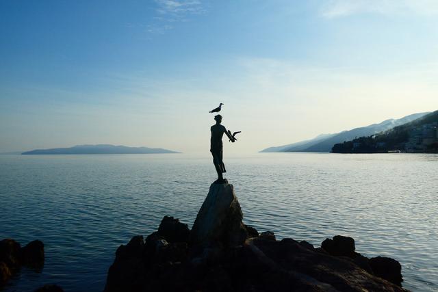 Woman with seagull on her in front of ocean