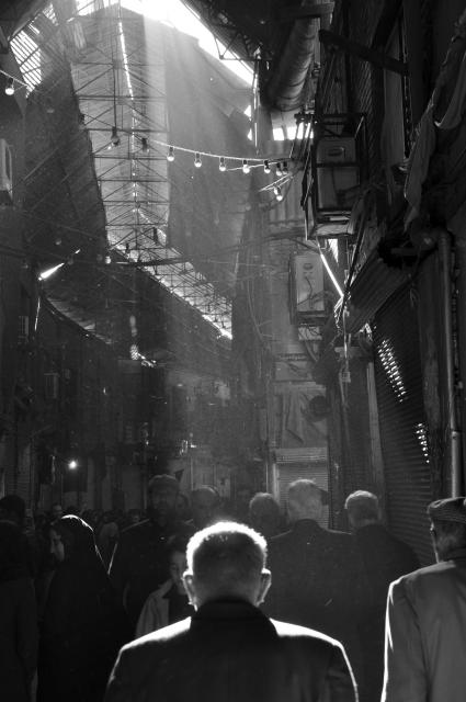 Light pouring in on a market street over the heads of shoppers