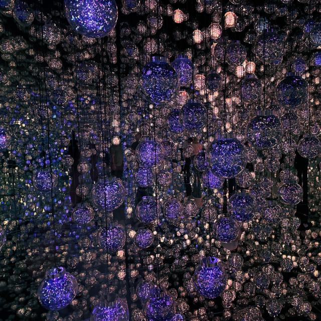 An immersive art installation by Yayoi Kusama, featuring numerous suspended spheres filled with purple lights, creating a dazzling and infinite mirror effect.