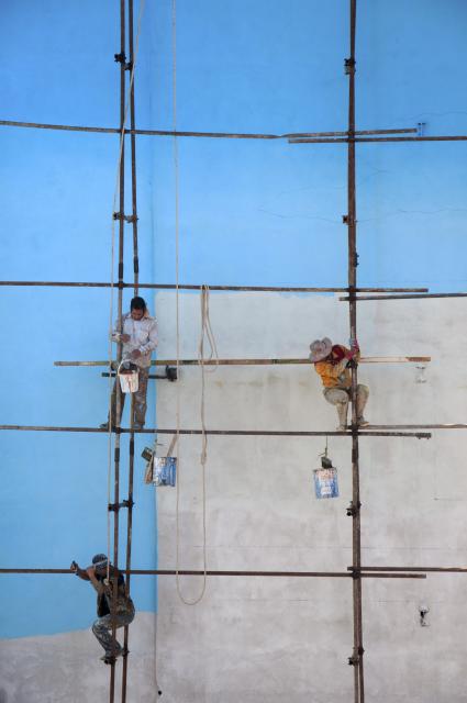 People on scaffolding painting a wall blue