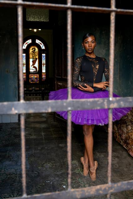 Ballerina poses behind bars in a room.