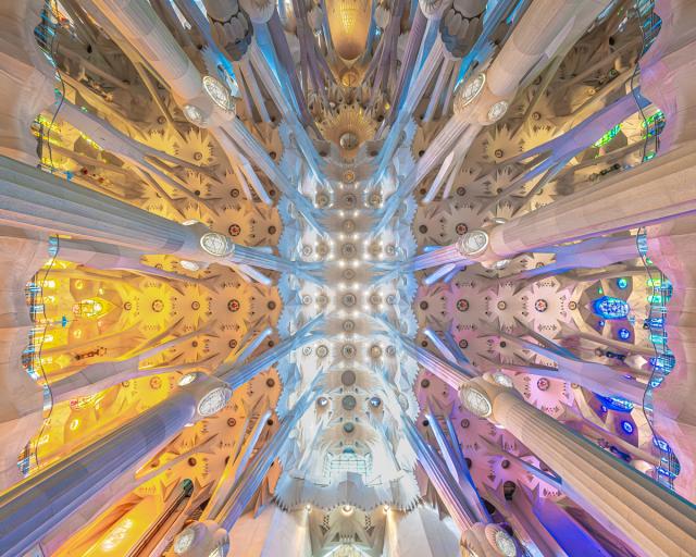 Intricate ceiling of the Sagrada Familia, featuring colorful stained glass and ornate architectural details with column structures extending upwards.