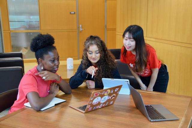 Three young people looking at a laptop screen inside a library