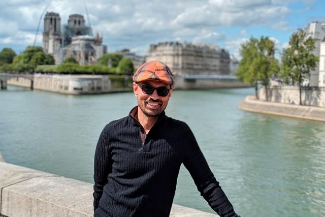 Man wearing sunglasses and cap with river in background.
