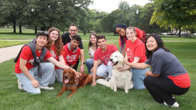 Group of smiling young students in Ohio State gear petting 2 dogs