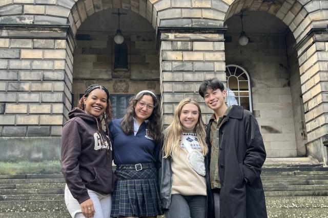 Four students smile in front of a European building