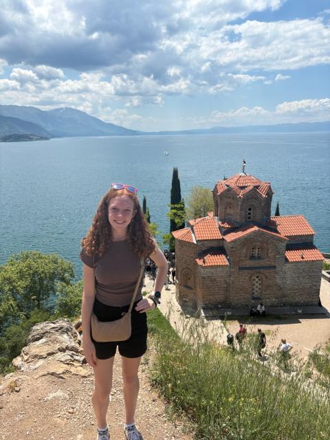 Student smiling on a coastline with building in background