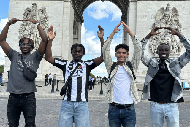 Four young men smile in front of an arch in France