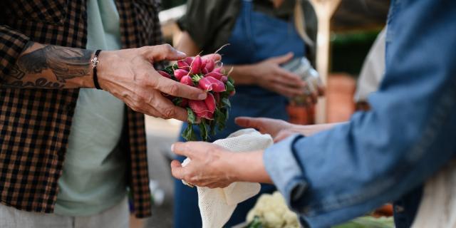 person handing another person produce at farmers market
