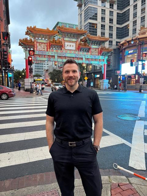 Man stands in street with Chinese gate behind him