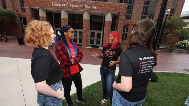 Group of 4 students chatting, one student's shirt reads "global engagement"