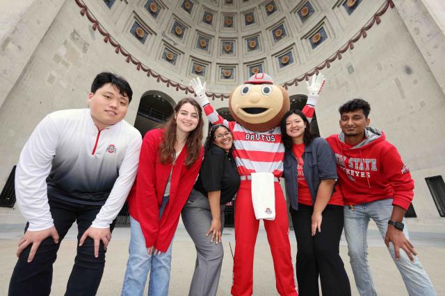 Students smile with Brutus Buckeye in front of Ohio Stadium.