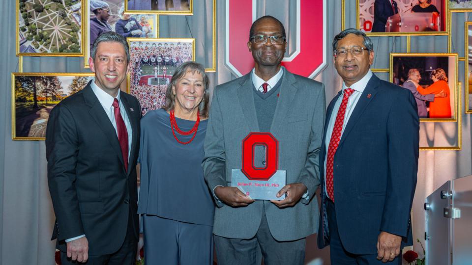 Three men and one woman in formal suits at award reception.