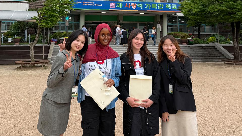 Four students stand in front of a school