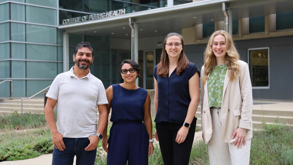 A male and three women pose outside of university building.