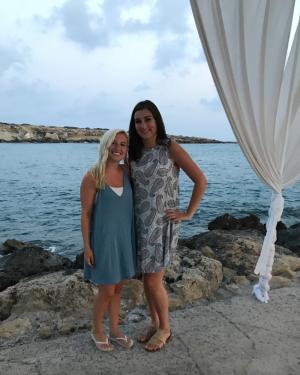 Two women pose in front of body of water.