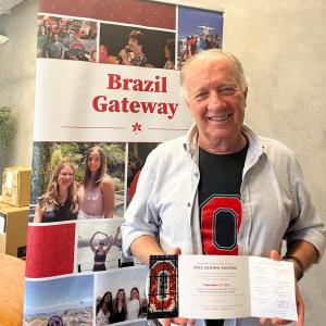 Man holding invitation in front of Brazil Gateway banner.
