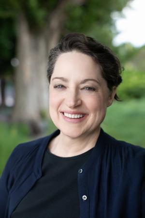 Portrait of a smiling person outdoors with trees in the background.