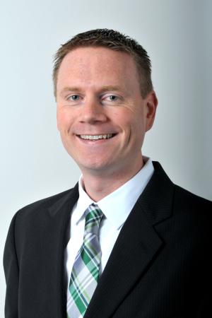 Professional portrait of a smiling person wearing a dark suit and a green striped tie against a light gray background.