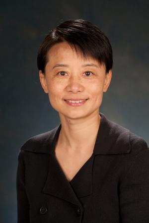 Official portrait of a person with short hair, wearing a dark blazer, against a mottled blue background.