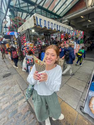 Woman smiling holding up ice cream cone in street setting.