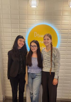 Three individuals smiling in front of a wall with a circular logo