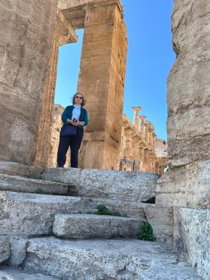 Woman standing among ruins of a Greek temple.