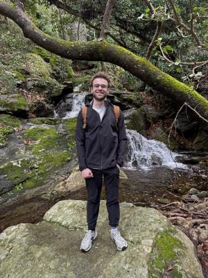 Student posing on a rock in a forest