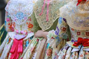 Three people in traditional Spanish dresses with elaborate lace and floral patterns during a cultural festival.