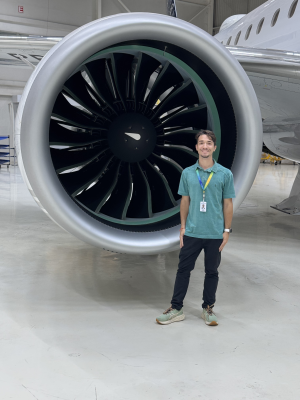 Caue poses for a picture in front of an airplane jet engine