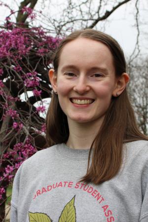 Female outdoor portrait wearing gray sweatshirt with flowers in background.
