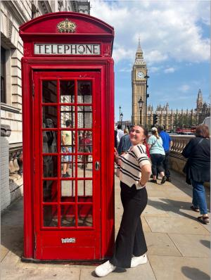 Woman posing by red British phone booth with Big Ben in background.